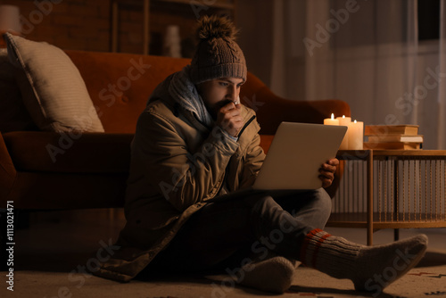 Frozen young man using laptop at home during blackout