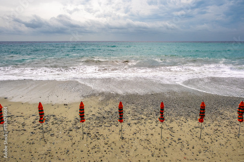 closed beach umbrellas on a rocky beach on a cloudy day in Italy photo