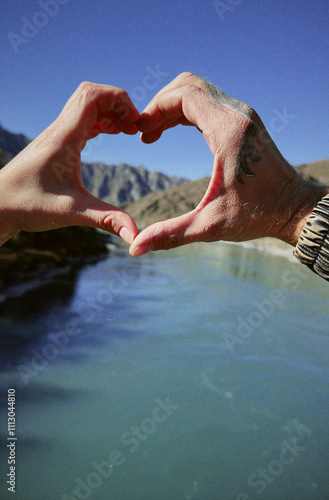 Couple making heart shape with hands framing mountain lake photo