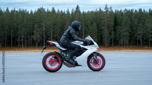 Fototapeta Naklejka Na Ścianę i Meble -  A young man in a black helmet and jacket rides a white and pink sport bike with red wheels on an empty parking lot on a summer evening