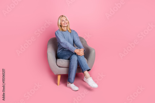 Full size photo of pretty retired lady relax sit soft armchair look empty space wear blue knitted outfit isolated on pink color background