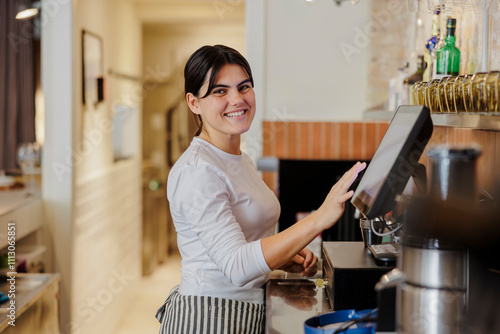 Cashier smiling while using a touchscreen cash register in a cafe photo