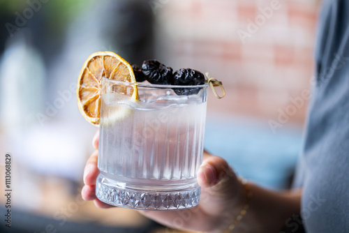 Woman holding plum vodka cocktail outdoors