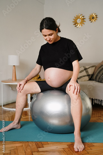 A pregnant woman sits on a large exercise ball photo