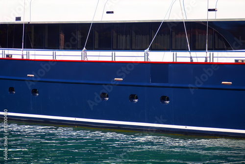 Boat side part view . Nautical vessel background. Side of a large boat featuring a dark blue hull with several circular portholes and a white upper section with large windows