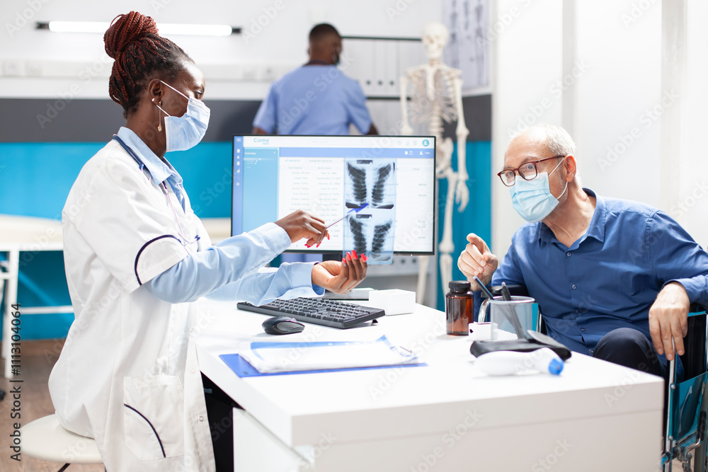 Caucasian pensioner patient in consultation with female physician, discussing xray results. African american doctor shows lung radiograph image to elderly man in wheelchair and explains the diagnosis. Caucasian pensioner patient in consultation with female physician, discussing xray results. African american doctor shows lung radiograph image to elderly man in wheelchair and explains the diagnosis.