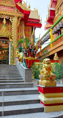 Golden lion statue stands guard at the foot of the steps leading to a vibrantly decorated buddhist temple photo