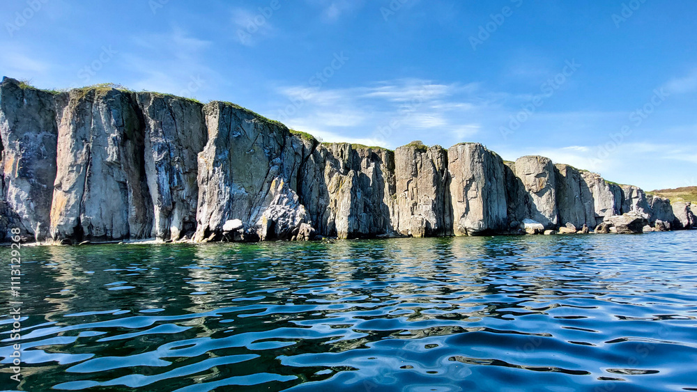 Naklejka premium Spectacular sight of a stunning rocky shore mirrored in the tranquil azure sea beneath a cloudless sky