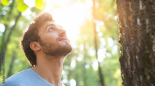 A young man gazes upward in a sunlit forest, reflecting on nature.