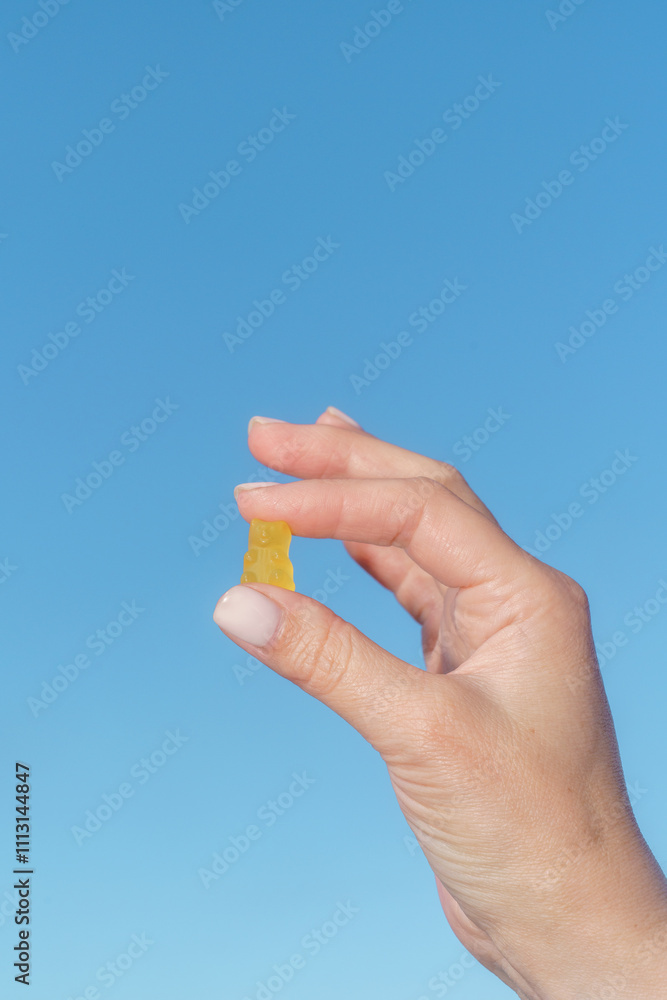 Hand Holding a Yellow Gummy Bear Against Blue Sky Hand Holding a Yellow Gummy Bear Against Blue Sky