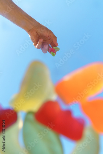 Hand holding colorful gummy candies with a bright blue sky background