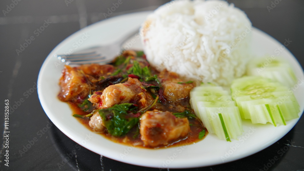 Plate of spicy Thai basil chicken stir-fry served with steamed white rice and fresh cucumber slices. Plate of spicy Thai basil chicken stir-fry served with steamed white rice and fresh cucumber slices.
