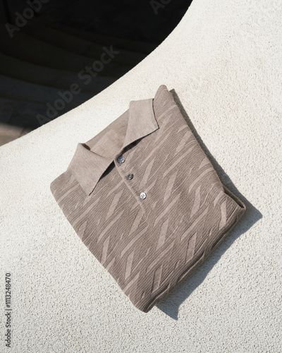 Folded light brown polo shirt on a textured white surface photo