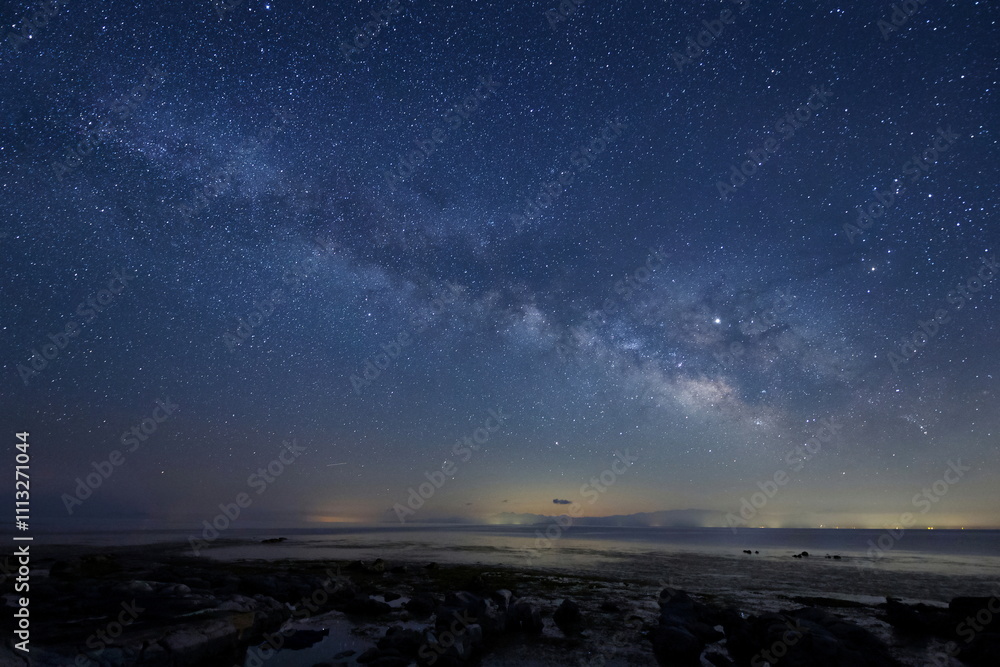 岩場の海岸の夜空に輝く天の川と能登半島の星々
