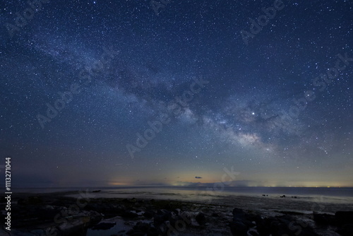 岩場の海岸の夜空に輝く天の川と能登半島の星々