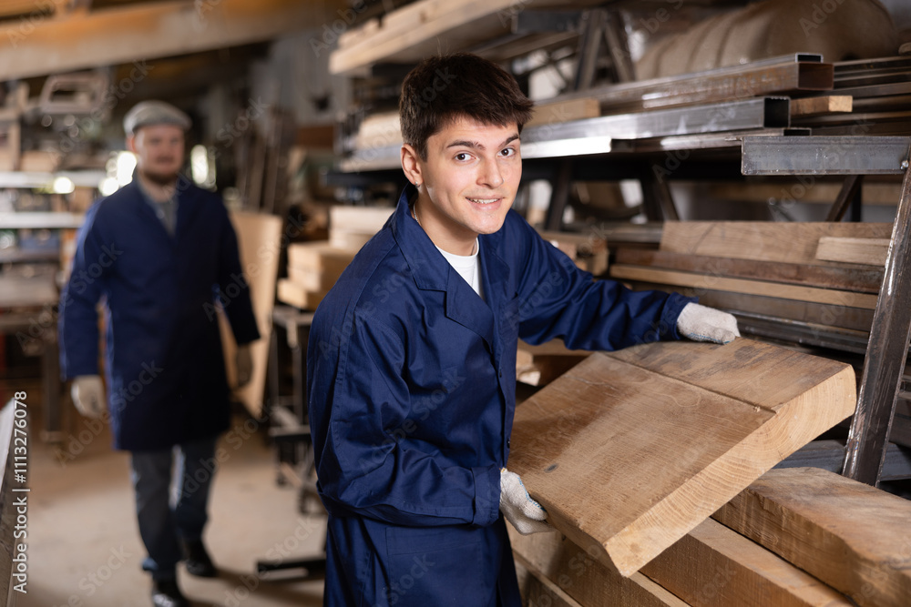 Young guy worker takes wooden plank from stack in wood workshop Young guy worker takes wooden plank from stack in wood workshop