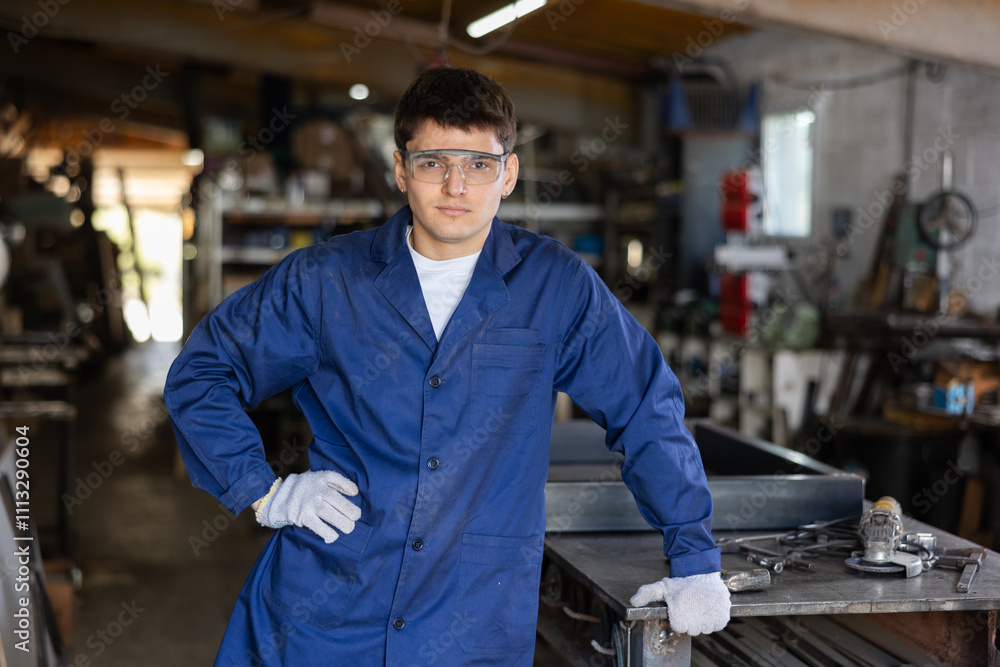Young male worker in uniform posing while working in workshop Young male worker in uniform posing while working in workshop