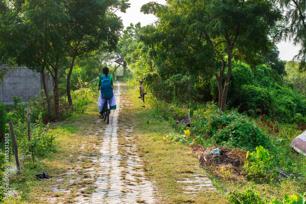 Obraz premium Teenage Girl Cycling to School on a Village Path in Rural India