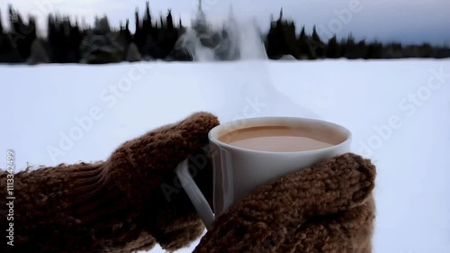 A close-up of warm mittens holding a steaming cup of hot chocolate outdoors