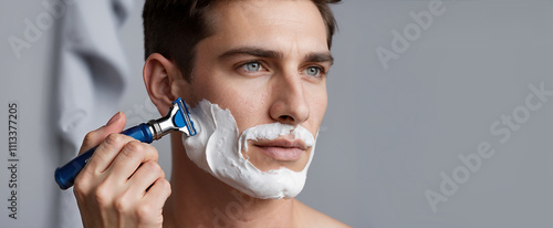 A man uses a razor to shave his face with shaving cream. For men's grooming, hygiene, and self-care campaigns.