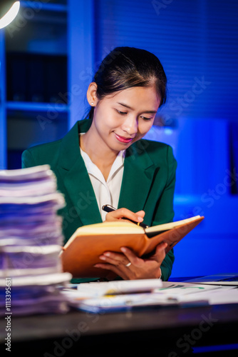 An Asian businesswoman works overtime,sitting at her desk at night, searching through numerous documents on her PC or laptop.Facing office problems,she also chats online while handling lots of work