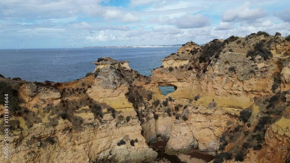 Aerial view of a rocky coastline in Portugal, featuring striking sandstone cliffs meeting the deep blue sea. The drone captures the rugged textures and dramatic formations under a sunny sky. Aerial view of a rocky coastline in Portugal, featuring striking sandstone cliffs meeting the deep blue sea. The drone captures the rugged textures and dramatic formations under a sunny sky.