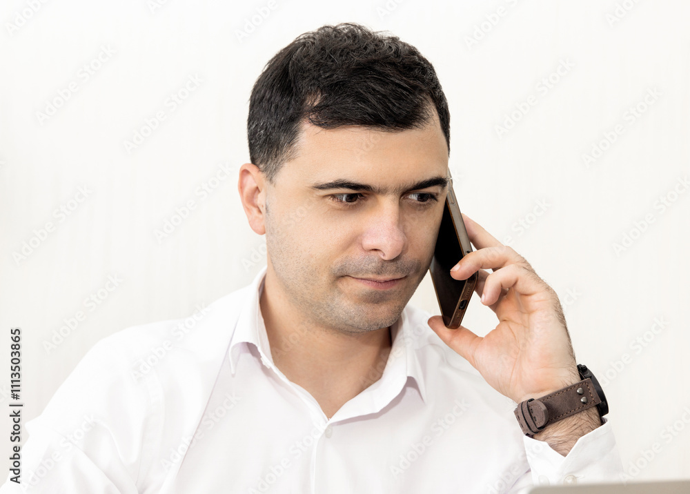 man working in office,talking at smartphone or having video call.guy with headphones is smiling,explain something,gesturing with hands. worker writing something in agenda.monstera leaf in background. man working in office,talking at smartphone or having video call.guy with headphones is smiling,explain something,gesturing with hands. worker writing something in agenda.monstera leaf in background.