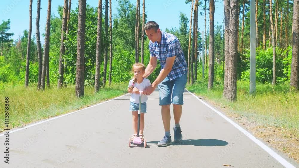 Father help child ride scooter at sunset. A father guiding a child's scooter. Child learning to ride scooter father support. Father help child ride scooter at sunset. A father guiding a child's scooter. Child learning to ride scooter father support.
