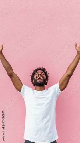 Joyful man celebrating with arms raised in front of a pink wall during daylight