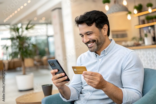 Happy Man Shopping Online with Mobile Phone and Credit Card in Modern Cafe Environment, Enjoying Convenient Banking Experience with Comfortable Atmosphere