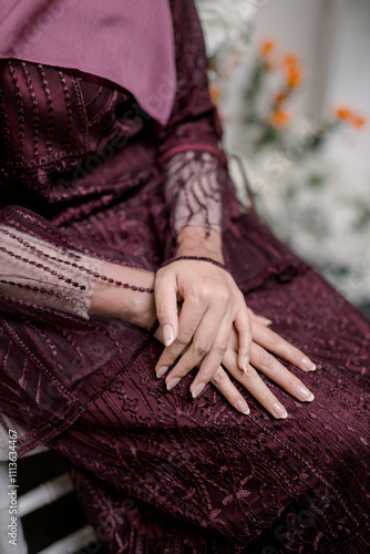 a woman sits wearing a dark red sharia dress with both hands on her lap