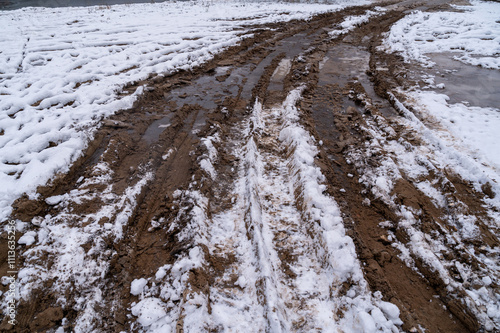 Muddy dirt road with snow patches and tire tracks in winter