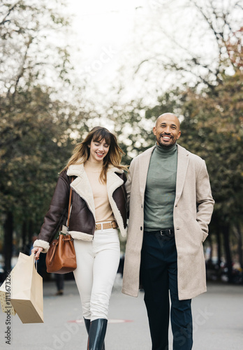 A joyful couple spending quality time shopping together, walking arm in arm down a tree-lined city street, carrying shopping bags, smiling, and enjoying each other's company. photo