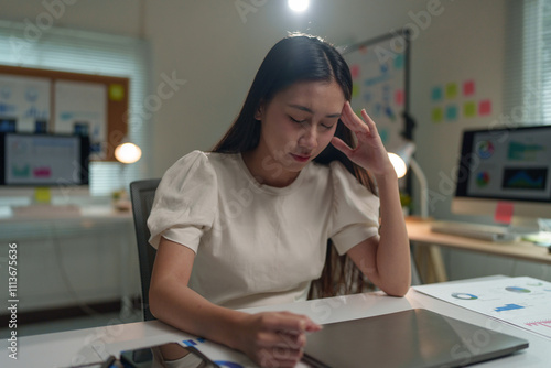 Asian businesswoman stressed, bored with financial documents, accounting problems, unapproved from working on laptop in modern office. Office syndrome concept. photo