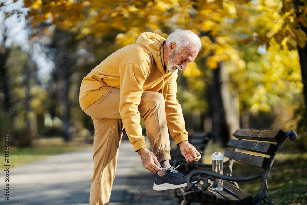 Fototapeta premium An old sportsman tying shoelace and preparing for outdoor practice in park.