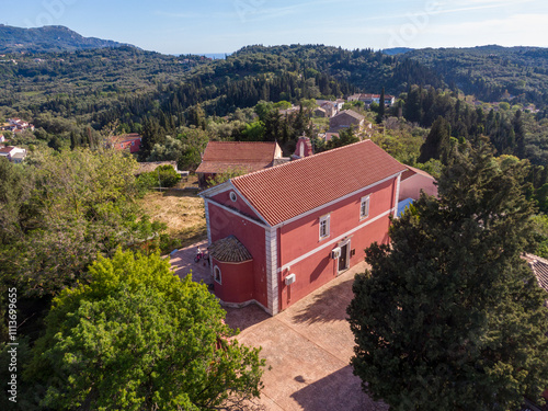 An aerial perspective reveals a charming pink church in Rachtades village  amidst a verdant setting.  The red roof contrasts with the surrounding greenery, creating a picturesque scene. Corfu,Greece photo