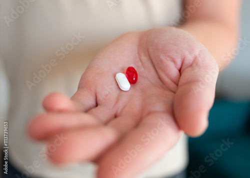 Close-up of a man's hand holding two pills red and white