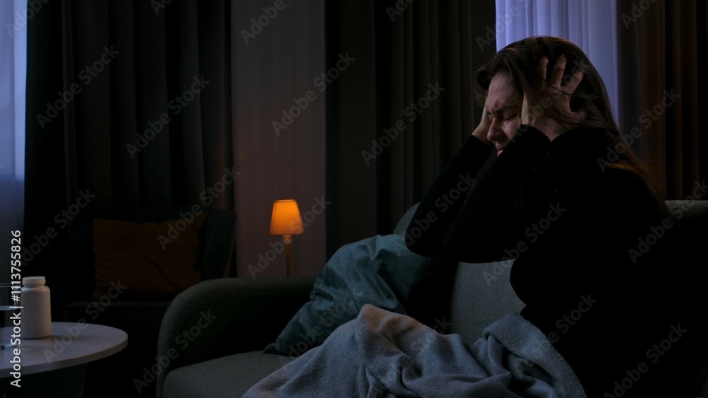 Woman suffering mental health issues, sitting on the sofa covered in blanket, depressed expression, holding head with hands, covers ears, side view. Woman suffering mental health issues, sitting on the sofa covered in blanket, depressed expression, holding head with hands, covers ears, side view.