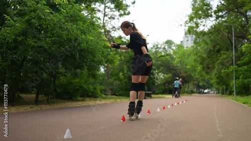 Wallpaper Mural Side view of an energetic teenage girl in a black sports summer uniform and knee pad skillfully hitting obstacles on roller skates during her hobby in the park Torontodigital.ca