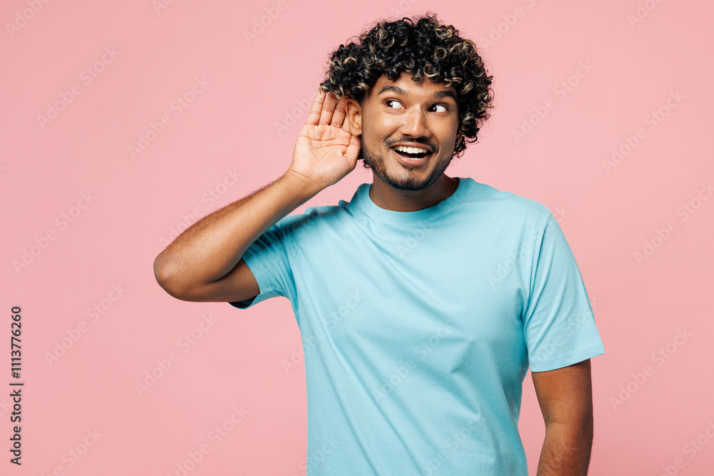 Young curious nosy happy Indian man he wear blue t-shirt casual clothes try to hear you overhear listening intently isolated on plain pastel light pink background studio portrait. Lifestyle concept. Young curious nosy happy Indian man he wear blue t-shirt casual clothes try to hear you overhear listening intently isolated on plain pastel light pink background studio portrait. Lifestyle concept.
