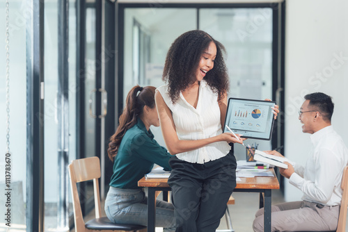 Successful Business Presentation: A young, enthusiastic businesswoman shares exciting data on a tablet during a lively team meeting.  Her colleagues react positively to the successful presentation. photo