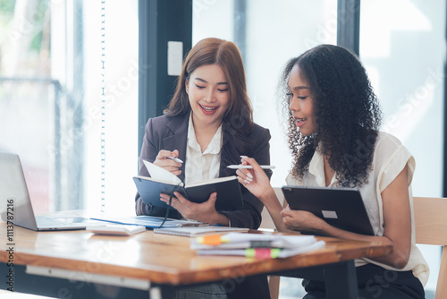 Collaborative Brainstorming:  Two diverse businesswomen engage in a productive discussion, their smiles reflecting a shared understanding and synergy. photo