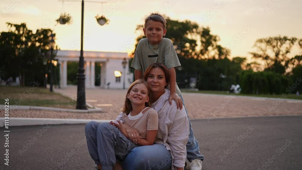 Portrait of a happy brunette woman in a shirt sitting with her daughter and son on a skateboard during a Happy Time in the Park in Summer Portrait of a happy brunette woman in a shirt sitting with her daughter and son on a skateboard during a Happy Time in the Park in Summer