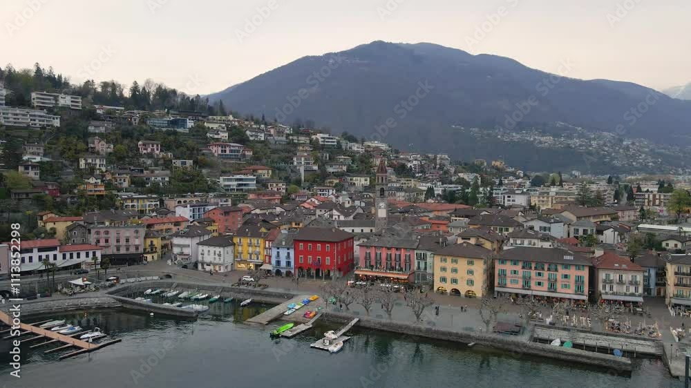 Colorful houses line the waterfront of Ascona, switzerland, nestled against the backdrop of alps mountains and lake Maggiore, Canton Ticino, Switzerland, drone orbiting shot Colorful houses line the waterfront of Ascona, switzerland, nestled against the backdrop of alps mountains and lake Maggiore, Canton Ticino, Switzerland, drone orbiting shot