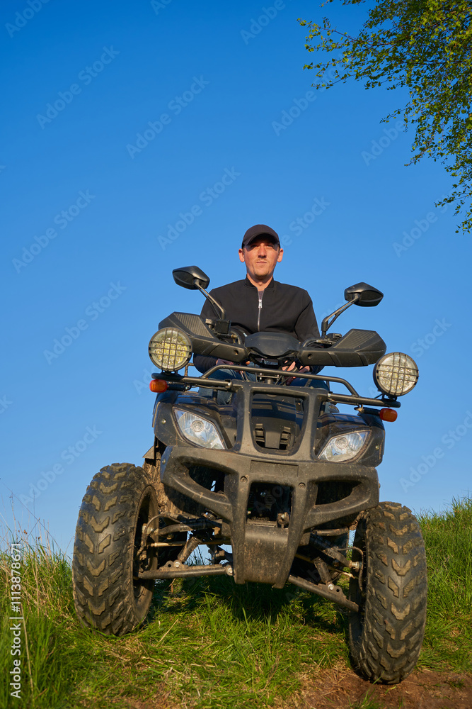 Fototapeta premium man sitting on a quad bike in nature, young guy riding a quad bike through the fields