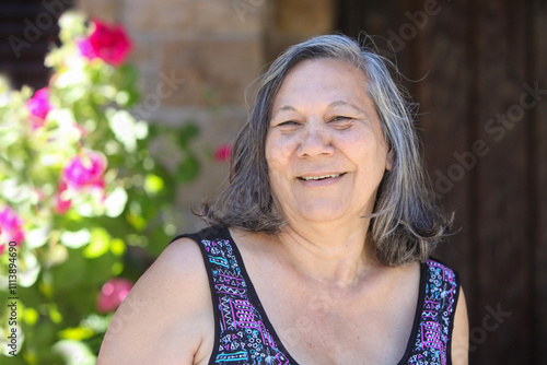 Canvastavla portrait of cheerful senior guarani latino woman in her garden by her house on s