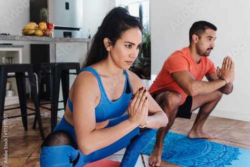 Young latin couple man and woman doing yoga on mat and meditating at home in Mexico Latin America. Positive active hispanic people in their apartment after exercising photo