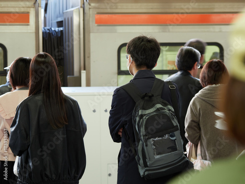 冬の朝の通勤時間の駅のホームで電車待ちの人々の姿