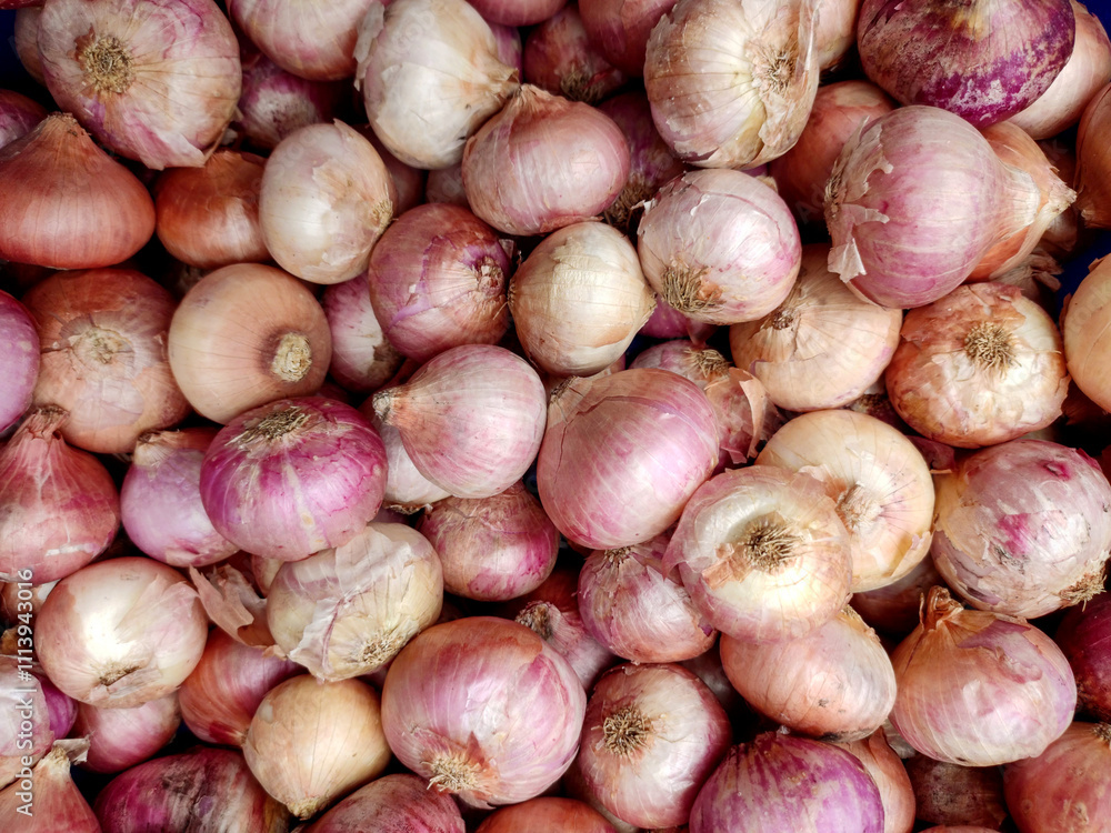 A close-up of freshly harvested red onions piled together. The vibrant reddish-purple skins and natural textures highlight their freshness and earthy appeal. A close-up of freshly harvested red onions piled together. The vibrant reddish-purple skins and natural textures highlight their freshness and earthy appeal.
