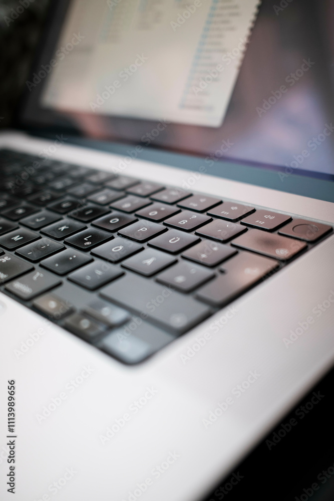 Close-up of a modern laptop keyboard with a blurred screen in the background. Close-up of a modern laptop keyboard with a blurred screen in the background.